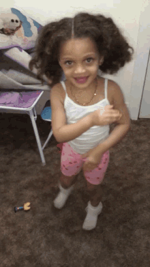 a little girl in a white tank top and pink shorts smiles for the camera