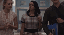 a group of people are walking down a hallway and one of them is wearing a plaid shirt