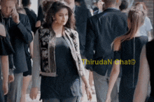a woman in a bomber jacket is walking through a crowd of people with a caption that says thiruda n chat