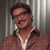 a man with glasses and a mustache is smiling and wearing a plaid jacket .