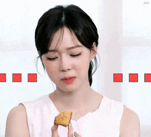a woman in a white tank top is holding a small piece of food in her hand .