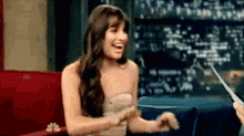 a woman in a strapless dress is sitting on a couch laughing