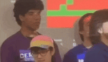 a man in a cerb shirt is talking to another man in a yellow hat .