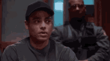 a man in a baseball cap is sitting in front of a police officer in a room .
