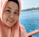 a woman wearing a pink hijab smiles in front of the ocean
