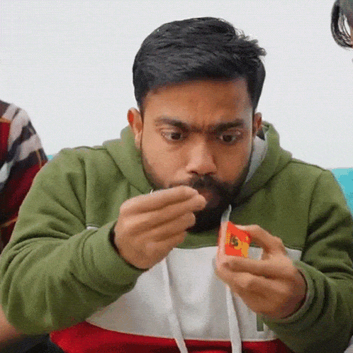 a man with a beard and a green hoodie is holding a small red object in his hand