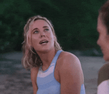 a woman in a blue tank top is talking to another woman while standing on a beach .