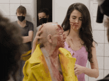 a woman in a pink tank top is standing next to a man in a yellow jacket with blood on his face