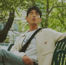 a man sitting on a park bench with his eyes closed wearing a white jacket and a t-shirt that says lm
