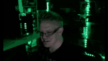 a man wearing glasses is smiling in a dark room with green lights behind him .