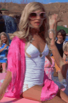 a woman in a white swimsuit and pink cardigan is sitting on a pink couch
