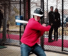 a man in a red hoodie is swinging a bat at a ball