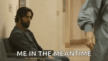 a man with a beard is sitting in a hospital chair and talking to another man .