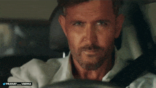 a man with a beard is sitting in a car with the name pranay on the bottom right