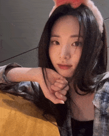 a woman wearing a plaid shirt and a bunny ear headband looks at the camera