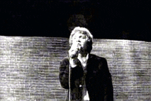 a man is singing into a microphone in front of a brick wall