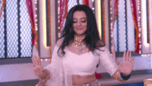 a woman in a white crop top is dancing in a room with her hands in the air .