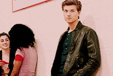 a man in a leather jacket is leaning against a wall with two women behind him