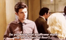 a man in a plaid shirt and tie is talking to a woman and says do you know that wildflower mural on the second floor