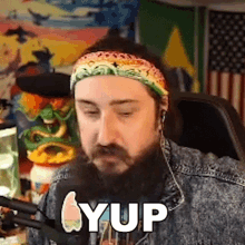 a man with a beard wearing a headband and headphones says yup in front of a microphone .