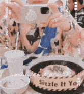 a person taking a picture of a plate of food with a sign that says sizzle it you on it