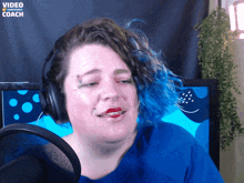 a woman wearing headphones is talking into a microphone with the words video coach visible in the corner