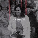 a woman in a white jacket is holding a microphone in front of a crowd that says tvduxae