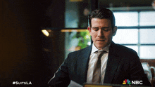 a man in a suit and tie is looking at a piece of paper with the nbc logo on the bottom