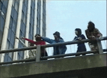 a group of people are standing on the edge of a bridge looking out at a building .