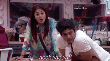 a man and a woman are sitting at a table and the man is saying acchaaaa