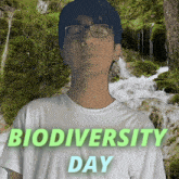 a man wearing glasses and a white shirt stands in front of a waterfall with the words biodiversity day above him