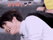 a man in a white shirt is laughing in front of a yellow mask with chinese writing on it