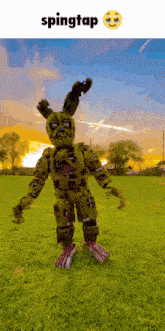 a picture of a springtrap standing in a grassy field with a sunset in the background