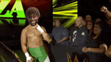 a wrestler in green shorts stands in front of a crowd with the letter a behind him