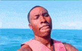 a man is sitting on a boat in the ocean wearing a life vest .