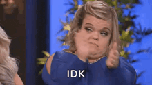 a woman in a blue dress is giving a thumbs up and making a funny face .