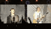 a man singing into a microphone while another man plays a guitar on stage