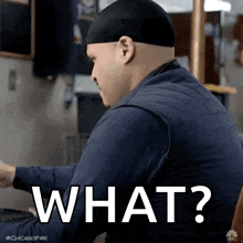a man wearing a hat is sitting at a table with the words `` what '' written on the screen .