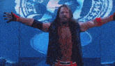 a wrestler with his arms outstretched is wearing a black vest and red gloves with the letter r on them