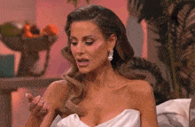 a woman in a white dress is sitting on a couch with her hand on her arm .