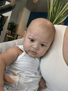 a baby with a sailboat on his shirt is being held by a woman in a white tank top