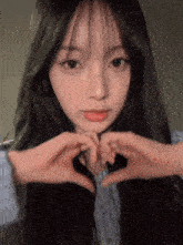 a girl with long black hair making a heart with her hands