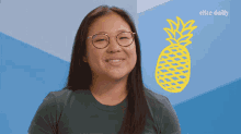 a woman wearing glasses is smiling in front of a pineapple that says elite daily on it