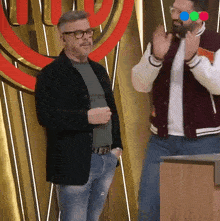 a man wearing glasses stands next to another man wearing a varsity jacket