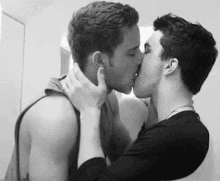 a couple of men are kissing in a black and white photo .