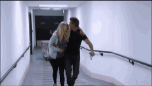 a man and a woman are walking down a hallway with a sign on the wall that says " emergency exit "