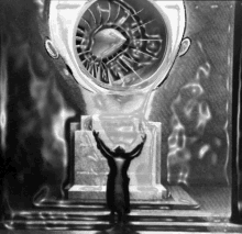 a black and white photo of a man standing in front of a large fan