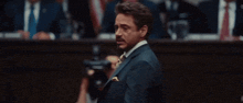 a man in a suit and tie is giving a peace sign while standing in front of a crowd .