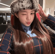 a woman wearing a fur hat and a plaid shirt is making a funny face
