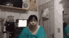 a woman in a green scrub top is standing in front of a mirror in a room .